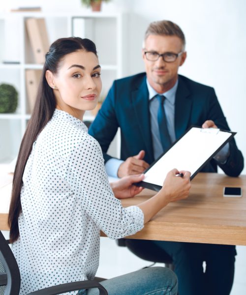 lawyer holding clipboard while female client signing contract and smiling at camera lawyer holding clipboard while female client signing contract and smiling at camera